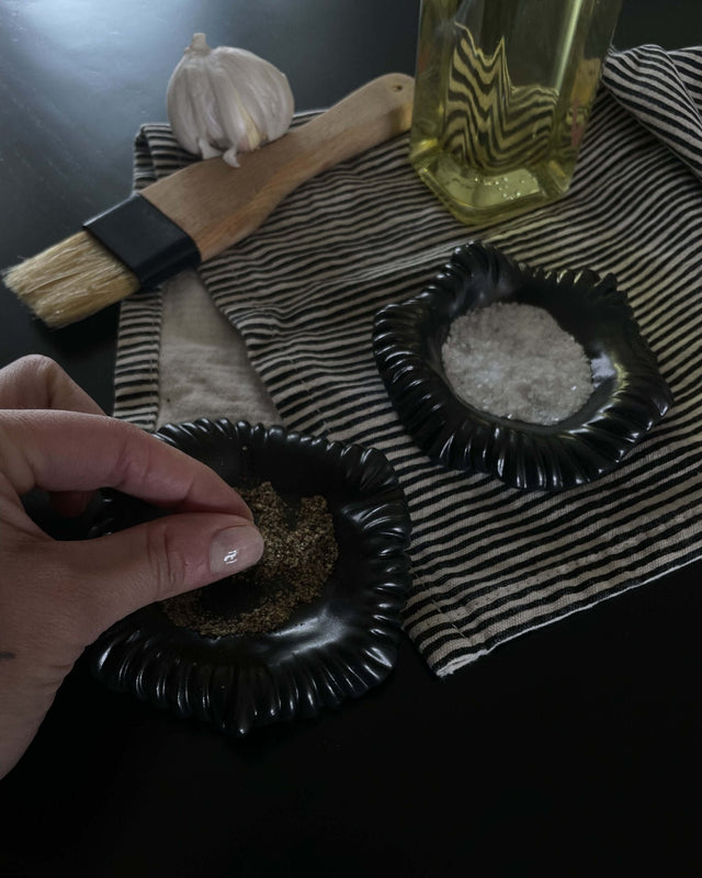 Small handmade ceramic salt and pepper dish, styled with striped cotton napkin and cooking essentials.